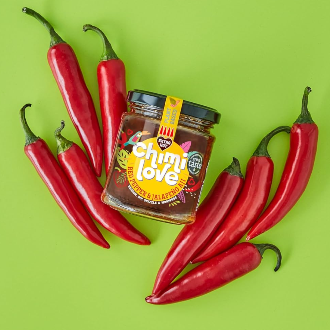 Jar of Chimi Love hot sauce surrounded by red peppers on a green background