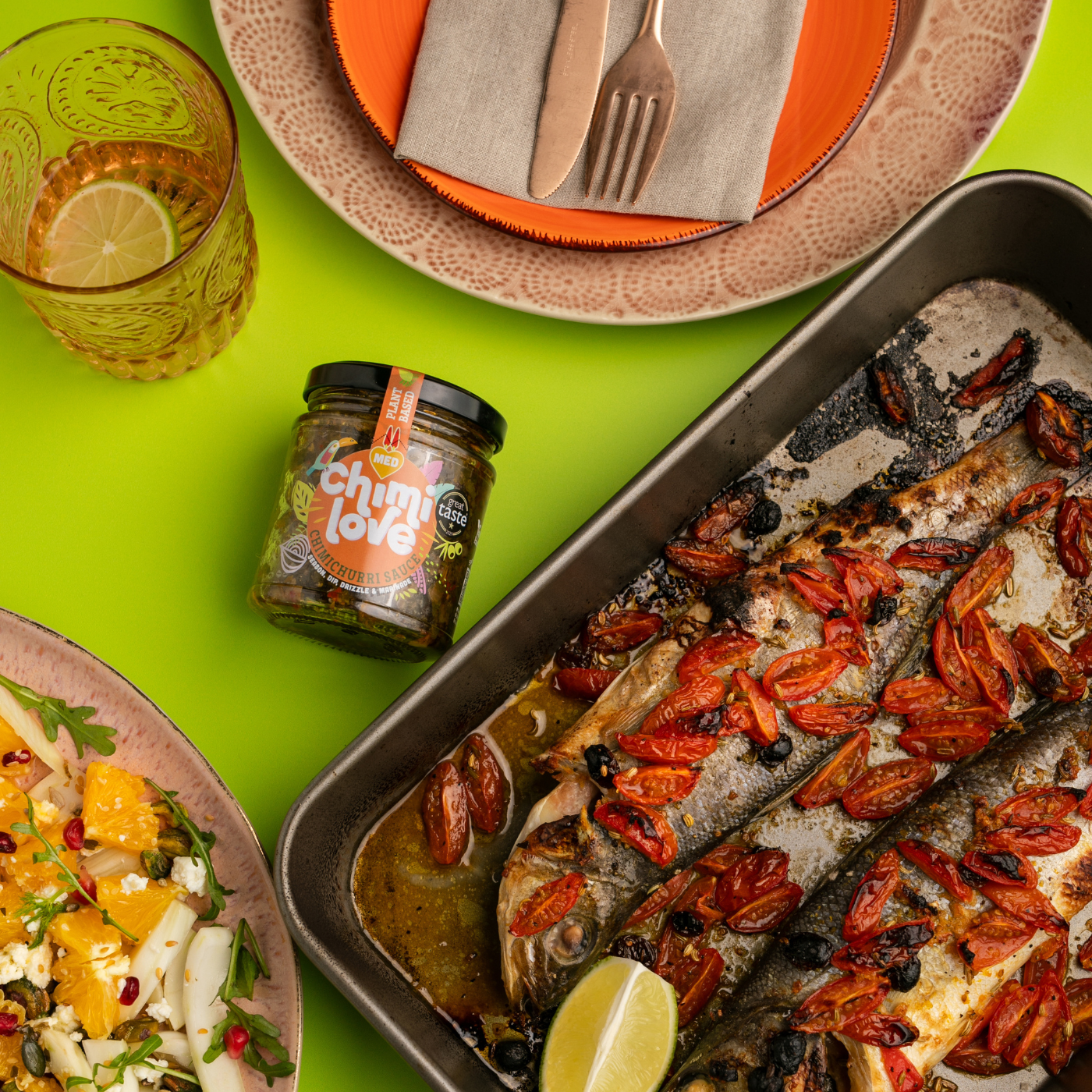 Fish dish with hot peppers and a jar of chimichurri on a green table.
