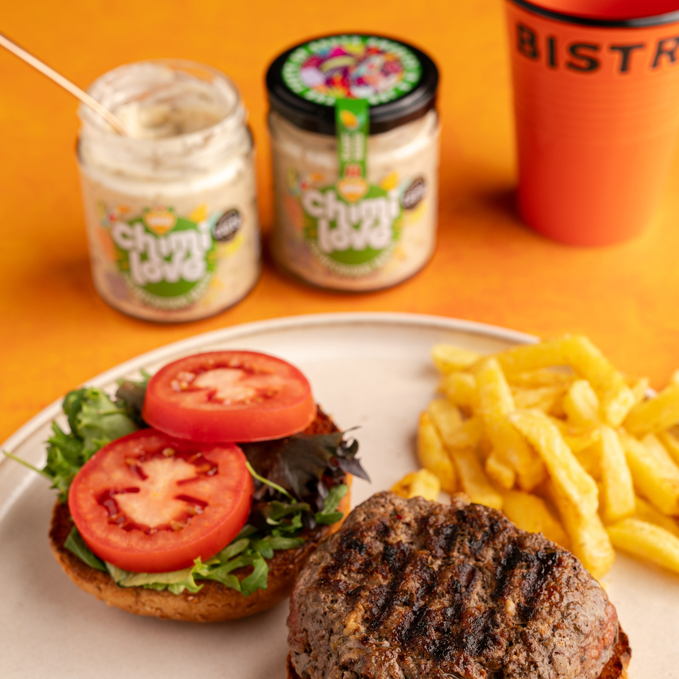 Two jars of Chimi Love Chimichurri Mayo served with a burger and chips.